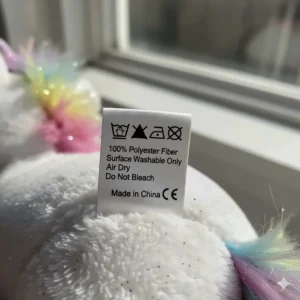 A photo of the sewn-in care and washing instructions label on the unicorn toy plush for easy cleaning.