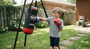 Happy boy practicing punches using a beginner kids boxing gloves and punching bag set in the backyard.
